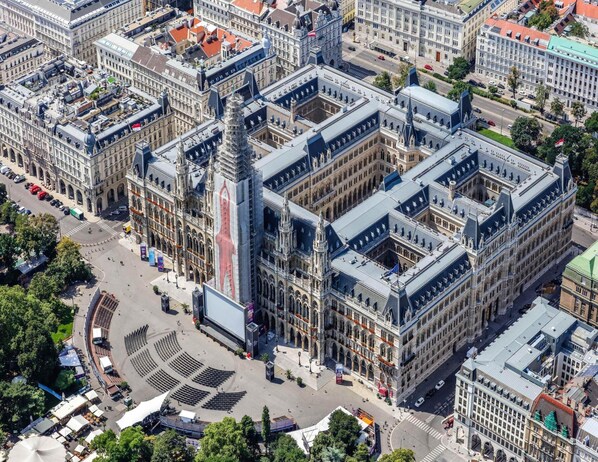A large, historic building with a central tower and multiple wings, surrounded by a cityscape.