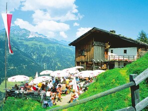 A wooden chalet with a balcony, surrounded by lush green hills and mountains.