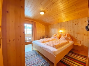 A wooden cabin bedroom with a bed, two bedside lamps, a window, and a view of the outdoors. - Holiday Home in St. Koloman Near Salzburg (Sankt Koloman)