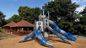A playground with two slides and a climbing structure, surrounded by sand and trees. - Holiday Home With a Terrace, Right on the Lake (Ryn)