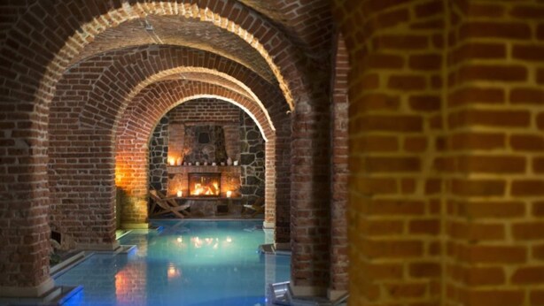 An indoor swimming pool with brick arches and a stone fireplace in the background. - Holiday Home With a Terrace, Right on the Lake (Ryn)