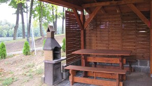 An outdoor patio with a stone barbecue and wooden picnic table. - Holiday Home With a Terrace, Right on the Lake (Ryn)