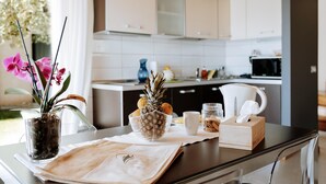 A kitchen with white cabinets, a pineapple bowl, a vase with pink flowers, and a tissue box on the counter. - Residence Nautic Resort San Carlo, Gargnano (Gargnano)