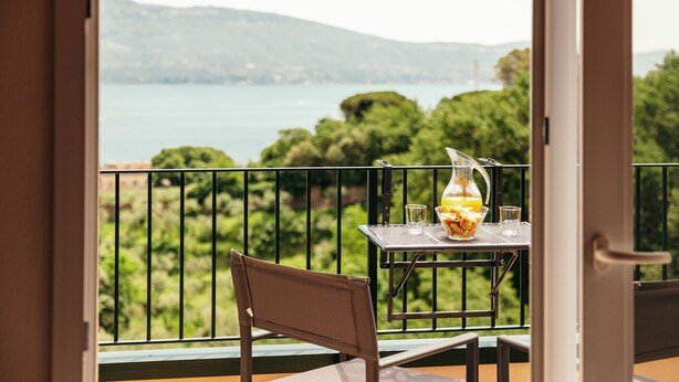 A balcony with a table, a chair, and a view of a lake and mountains. - Residence Nautic Resort San Carlo, Gargnano (Gargnano)