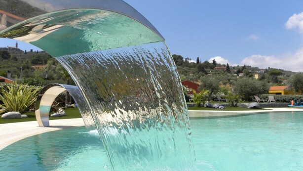 A pool with a clear water feature and a curved glass structure.