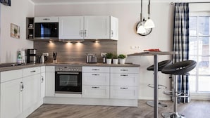 A modern kitchen with white cabinets, stainless steel appliances, and a bar stool. - Luxushaus Boddenkuste mit Sauna (Fuhlendorf)