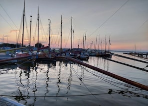 Ein Yachthafen mit mehreren vertäuten Booten, ruhigem Wasser und einem Sonnenuntergang im Hintergrund.