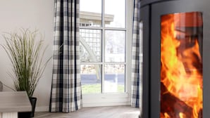 A room with a large window, plaid curtains, a potted plant, and a wood-burning stove. - Luxushaus Boddenkuste mit Sauna (Fuhlendorf)