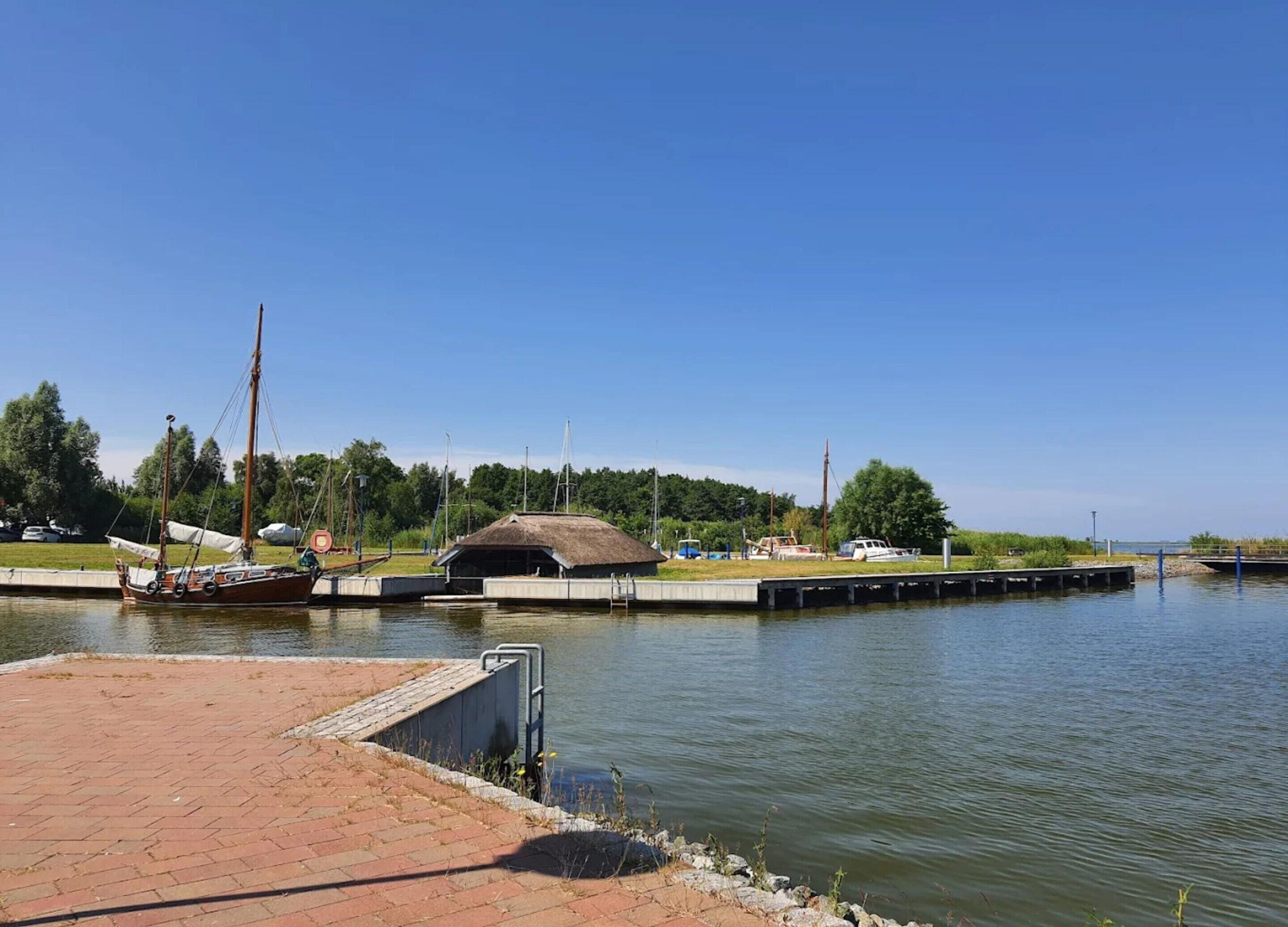 A calm waterfront with a dock, a boat, and a small building with a thatched roof.