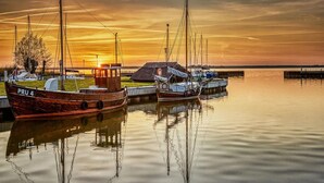 A calm harbor with boats docked, a small building, and a sunset in the background. - Luxushaus Boddenkuste mit Sauna (Fuhlendorf)