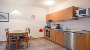 A compact kitchen with wooden cabinets, a microwave, a dishwasher, and a dining area with a table and chairs. - Ferienwohnung im Dunenpark Binz (Binz)