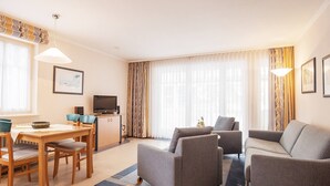 A modern living room with a sofa, two armchairs, a dining table with chairs, a television, and a cabinet. - Ferienwohnung im Dunenpark Binz (Binz)