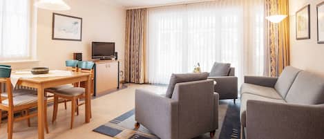 A modern living room with a sofa, two armchairs, a dining table with chairs, a television, and a cabinet.