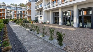 Un moderno edificio residencial de varios pisos con balcones, un camino pavimentado y una zona ajardinada.