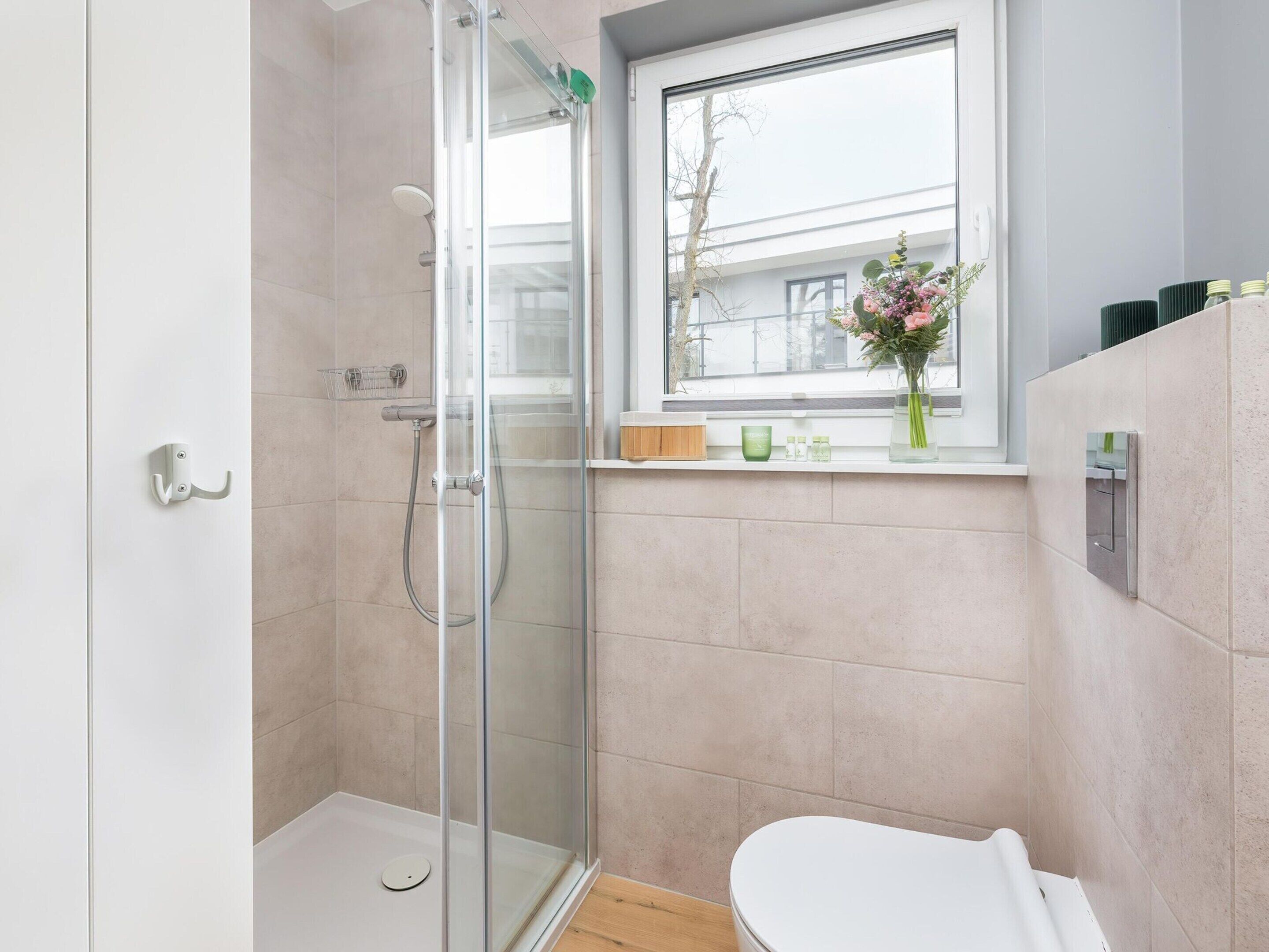 Un baño moderno con ducha de vidrio, inodoro y ventana con vista a edificios.