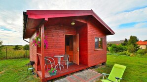 A small red wooden cabin with a porch, a table, and two chairs. - Cottage in Rusinowo Near Seaside Beach (Postomino)