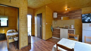 A wooden cabin with a dining area, kitchen, and a bed. - Cottage in Rusinowo Near Seaside Beach (Postomino)