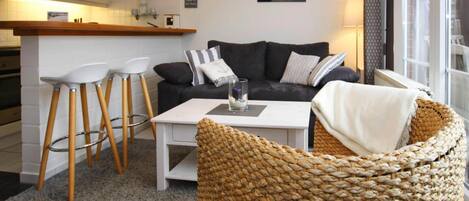 A modern living room with a sofa, two bar stools, a coffee table, and a wicker chair.