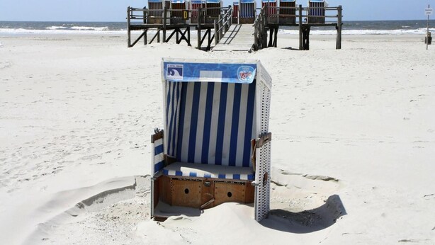 A beach with a row of beach chairs and a single empty beach chair in the foreground. - Ferienwohnung, Garding (Garding)