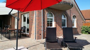 Un bâtiment en briques doté de deux espaces extérieurs aménagés pour s’asseoir, d’un parasol rouge et d’un vélo.