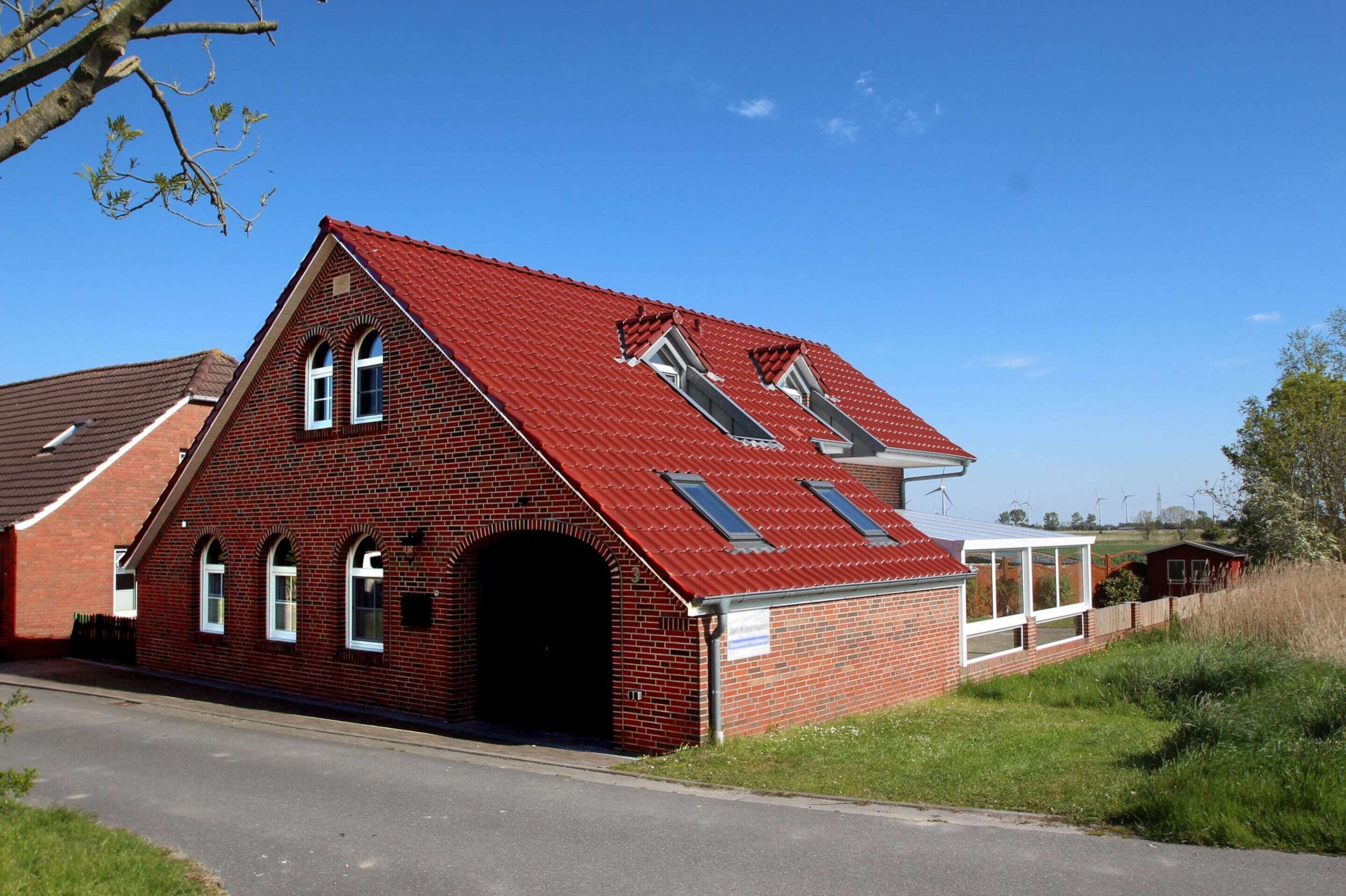 A red brick building with a sloped roof, a central arched doorway, and two skylights.