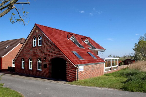 A red brick building with a sloped roof, a central arched doorway, and two skylights.