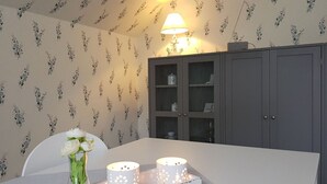 Un coin repas avec une table blanche, un vase rempli de fleurs blanches et deux bougies allumées.