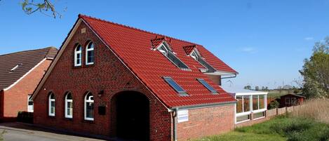 A red brick building with a sloped roof, a central arched doorway, and a small attached structure with windows.