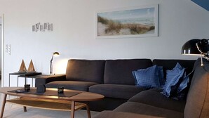 Un salon moderne avec un canapé d’angle, une table basse et un tableau représentant une scène de plage.