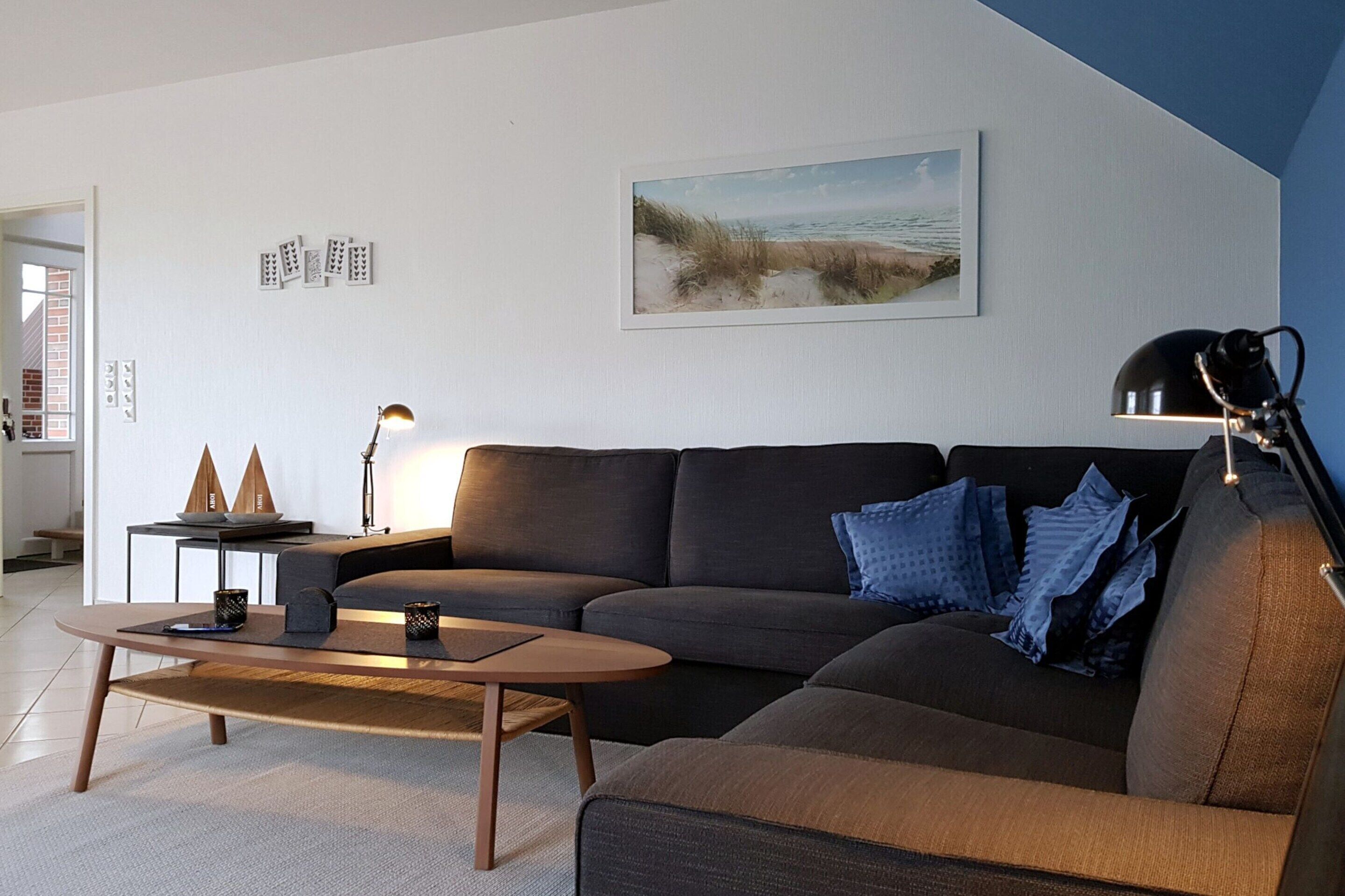 Un salon moderne avec un canapé d’angle, une table basse, une lampe et un tableau encadré au mur.