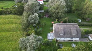 Et kystlandskab med et fyrtårn, et hus med stråtækt tag og frodig vegetation.