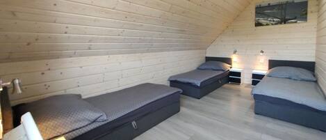 Una camera da letto soffitta accogliente e piccola, con pareti in legno, due letti singoli, un tavolino e un comodino.