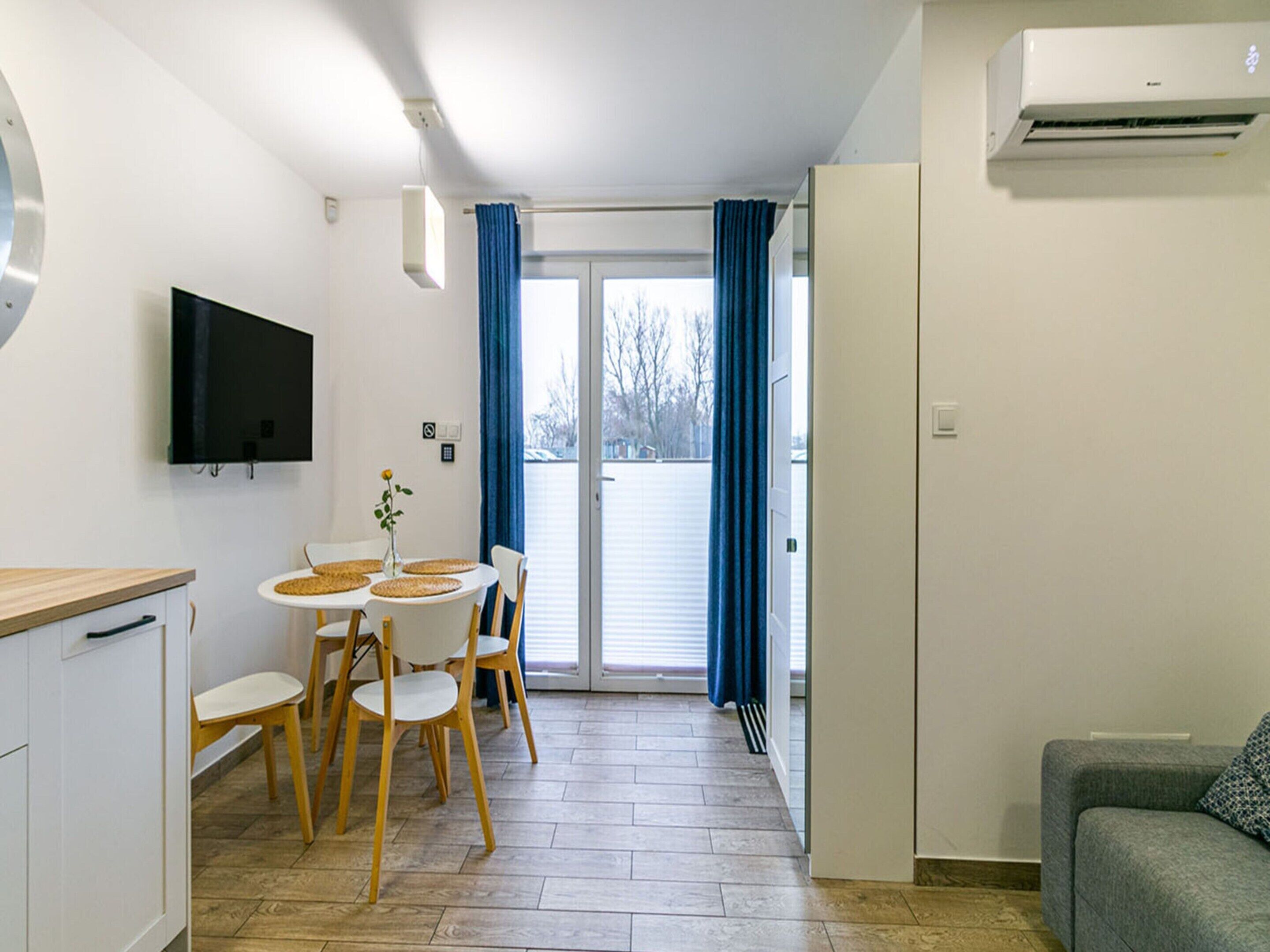 Eine moderne Küche mit Essbereich, einem Flachbildfernseher und einer Glasschiebetür, die auf einen Balkon führt.