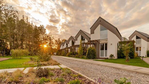 Ett modernt bostadskomplex med flera hus, en grusuppfart och en välskött trädgård med olika typer av växter.