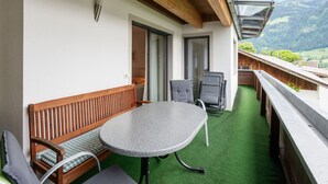 A balcony with a wooden bench, a table, and chairs, overlooking a mountainous landscape. - Apartment in Fugen Near Spieljochbahn (Fuegen)