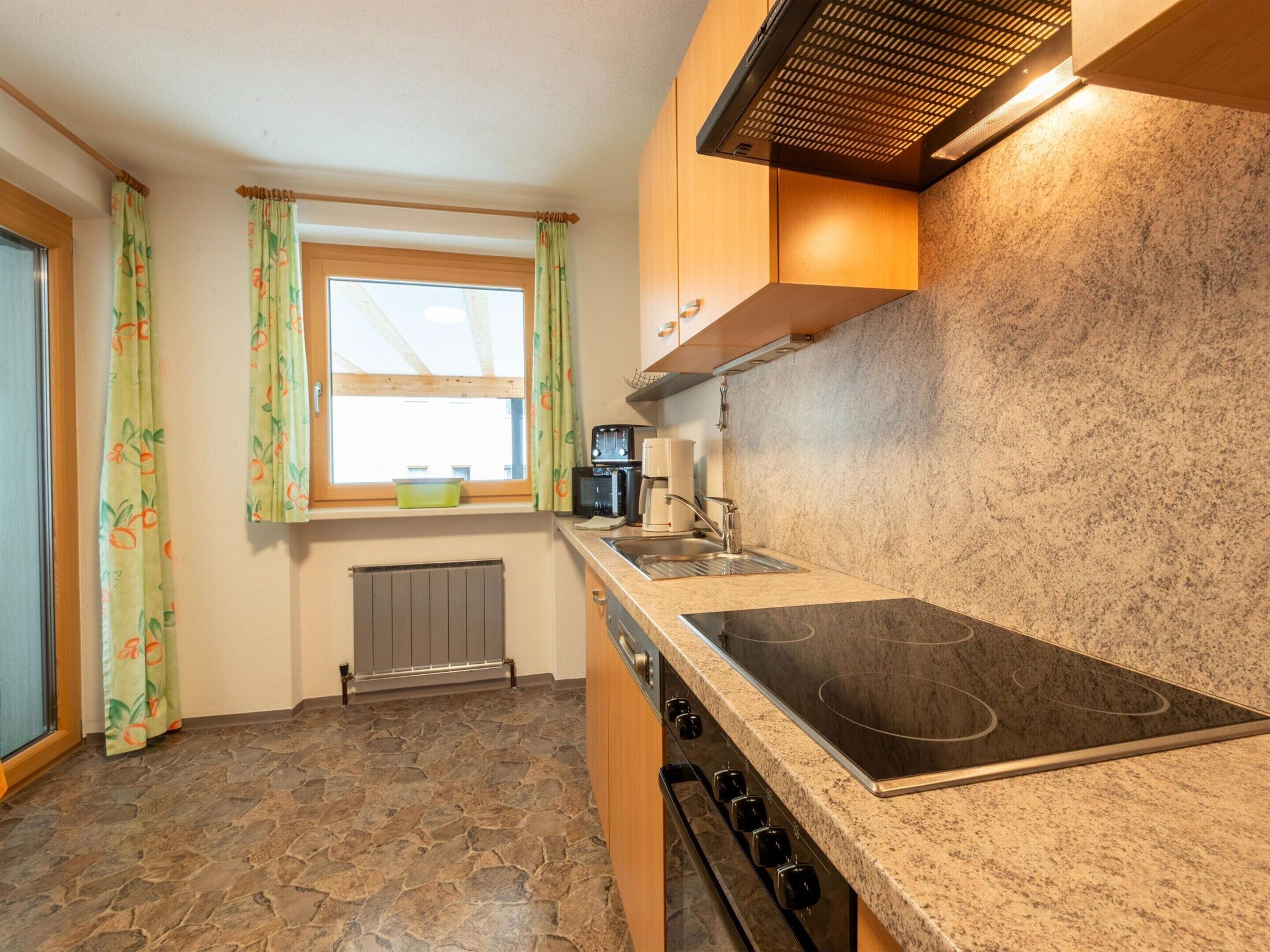 A kitchen with a stone floor, a built-in stove, a window with curtains, and a radiator.