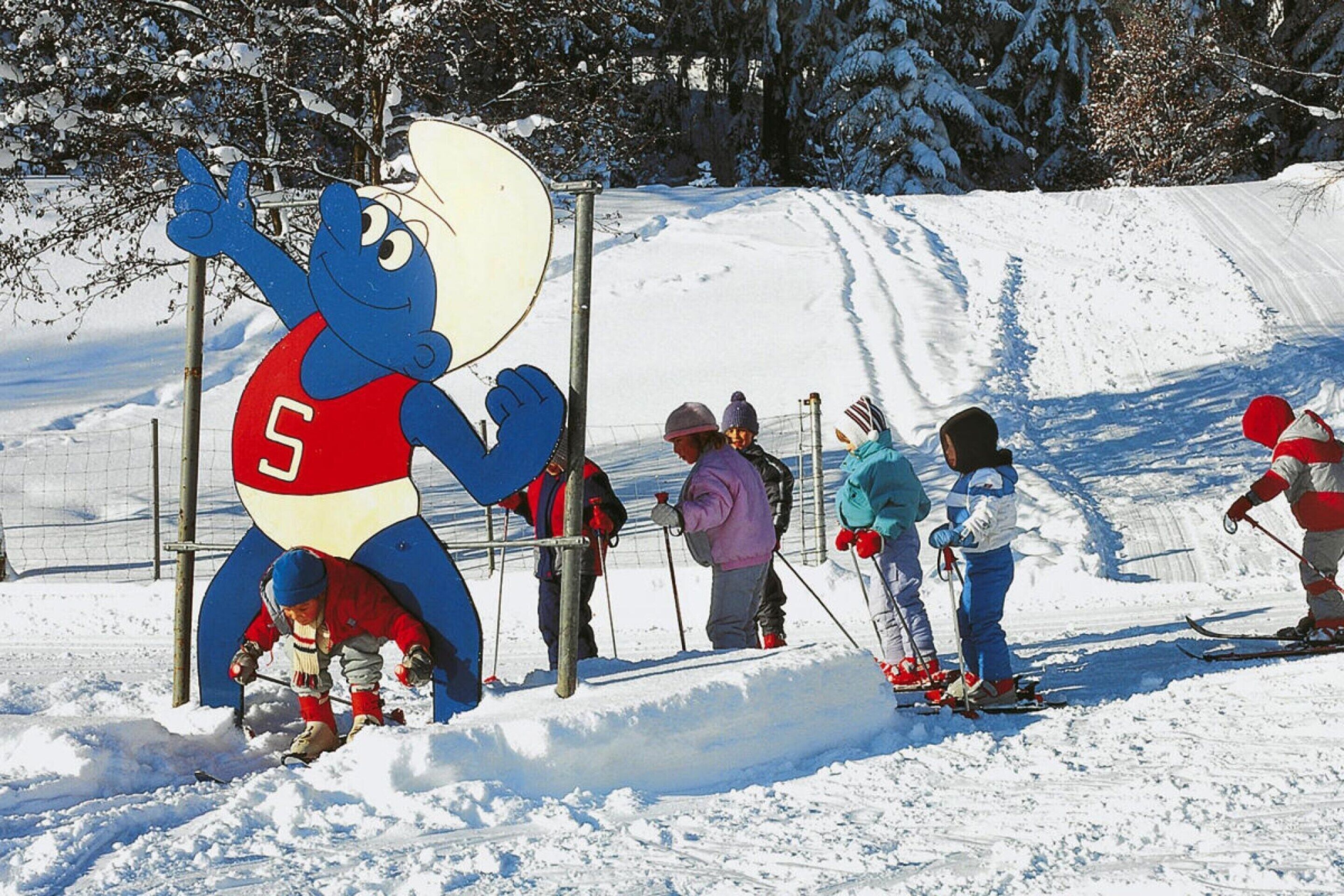 A mascot figure and skiers on a snowy slope.