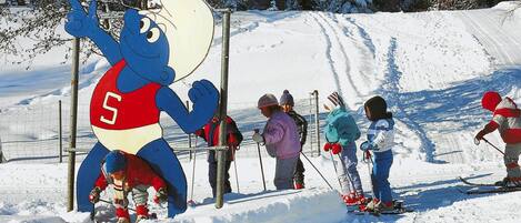 A mascot figure and skiers on a snowy slope.