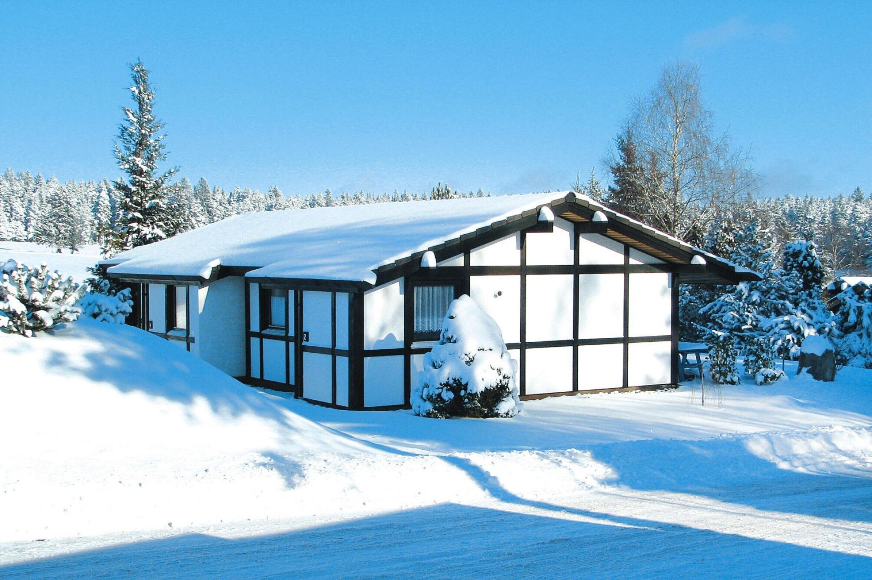 Ein mit Schnee bedecktes Haus mit einem großen Fenster und einer Holzterrasse.