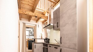 A modern kitchen with grey cabinets, wooden beams, and a wooden floor.