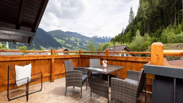 A wooden deck with wicker furniture and a table, overlooking a mountainous landscape.