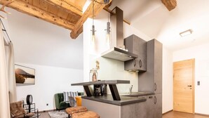 A modern kitchen with a central island, bar stools, a coffee machine, and a dining area with a sofa and chairs.