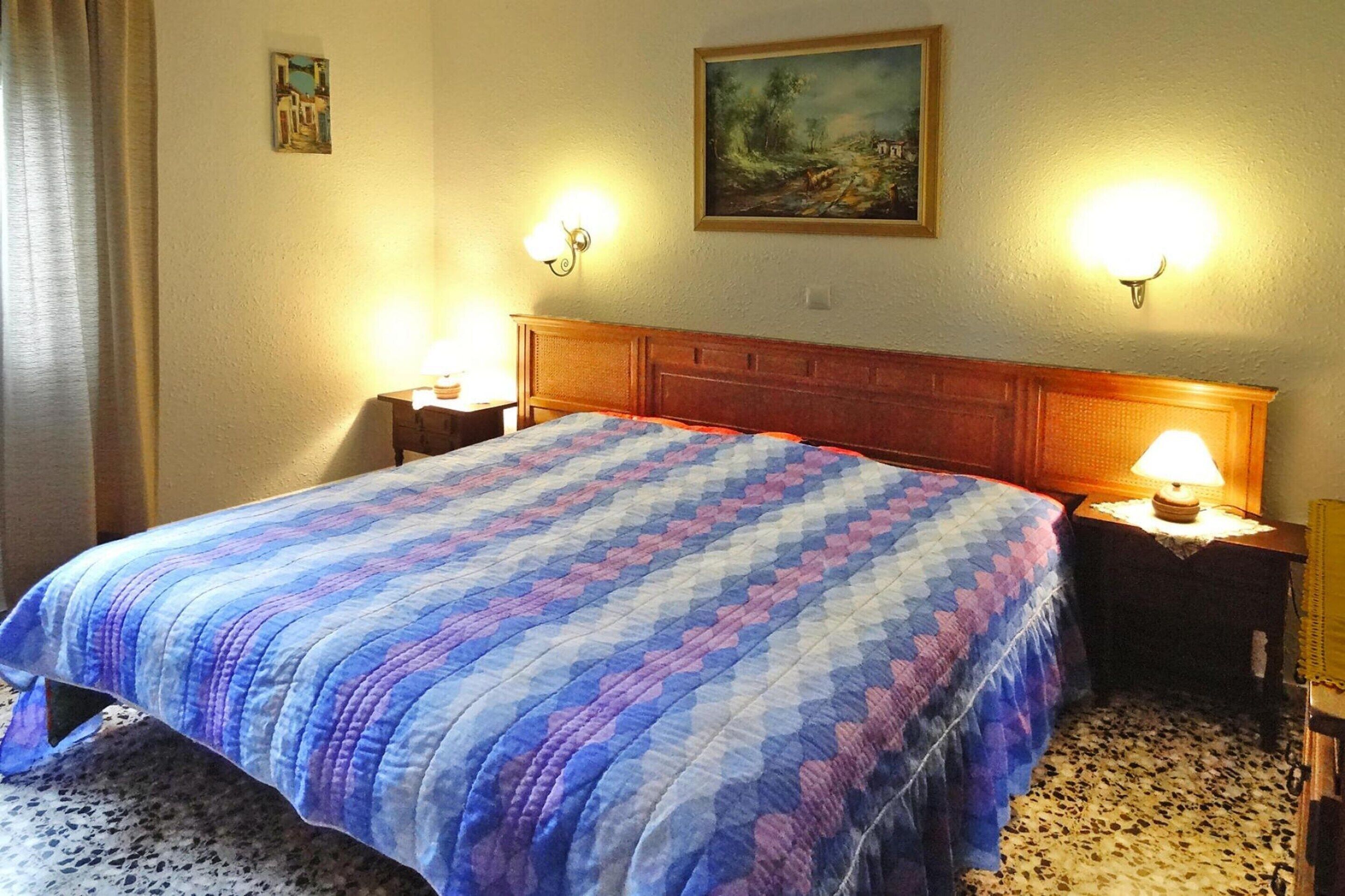 Una habitación de hotel con una cama grande, dos lámparas de noche, un cuadro en la pared y piso alfombrado.