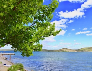 A lakeside view with a clear sky, calm water, and a distant hill. - Apartment in Bilice Near Krka National Park (Bilice)