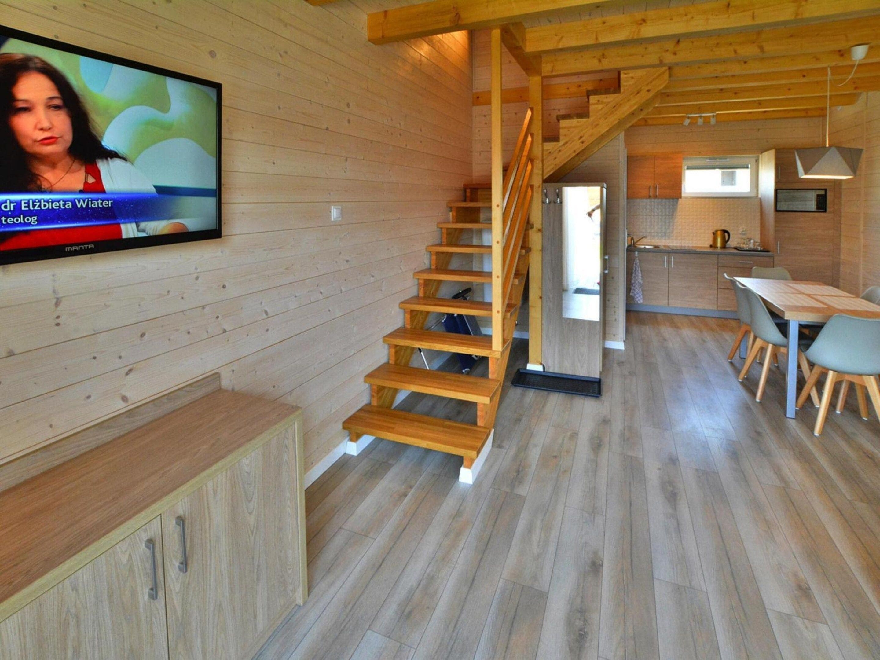 Un interior de madera con un televisor montado en la pared, una escalera, un comedor y una cocina.