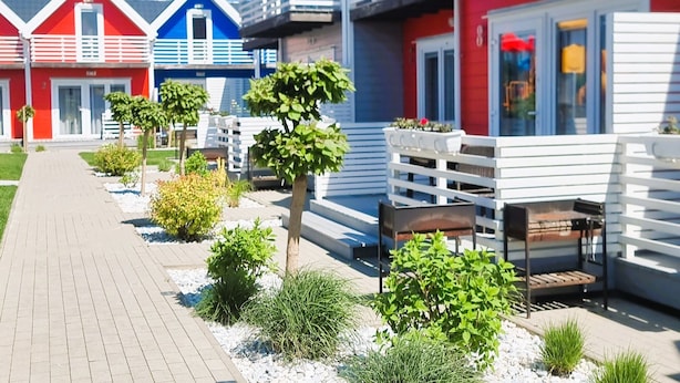 A row of colorful seaside cottages with a paved walkway and small plants. - Cottage in Sarbinowo Near Seaside Beach (Mielno)