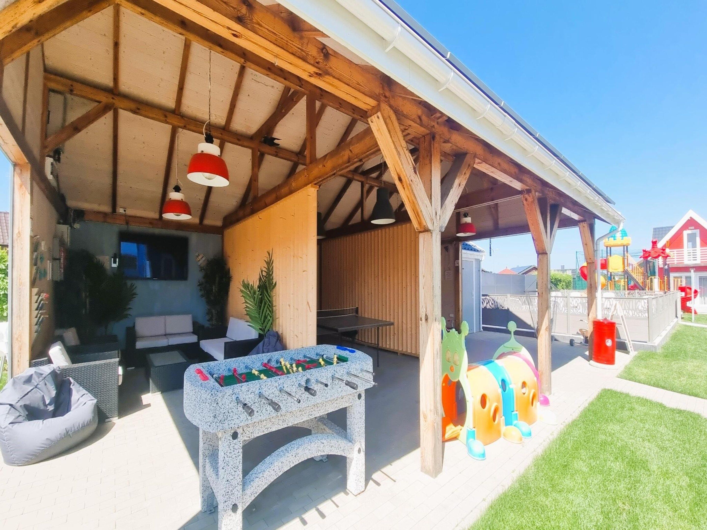 Un área de estar al aire libre con mesa de futbolín, un patio cubierto y una zona de juegos para niños.