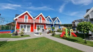 A row of colorful houses with a playground in the foreground. - Cottage in Sarbinowo Near Seaside Beach (Mielno)
