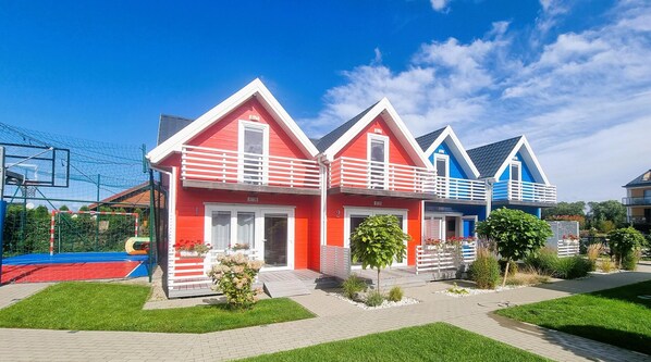 A row of colorful houses with a sports court in the background. - Cottage in Sarbinowo Near Seaside Beach (Mielno)