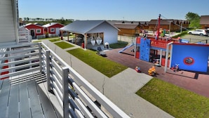A playground with slides and swings, a small building, and a fenced area with a red and blue structure. - Cottage in Sarbinowo Near Seaside Beach (Mielno)